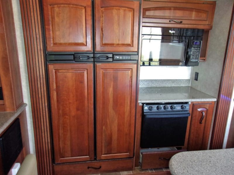 View of fridge, microwave, and dishwasher in small camper automobile - find more private vehicles up for sale at Maltz Auctions